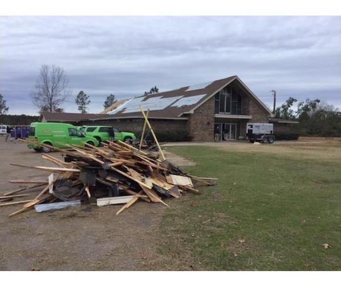 Pile of wood boards and home in the background with tarped roof