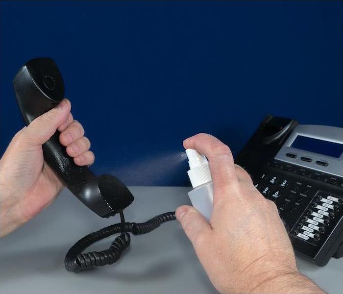 hands spraying a liquid on a black office phone